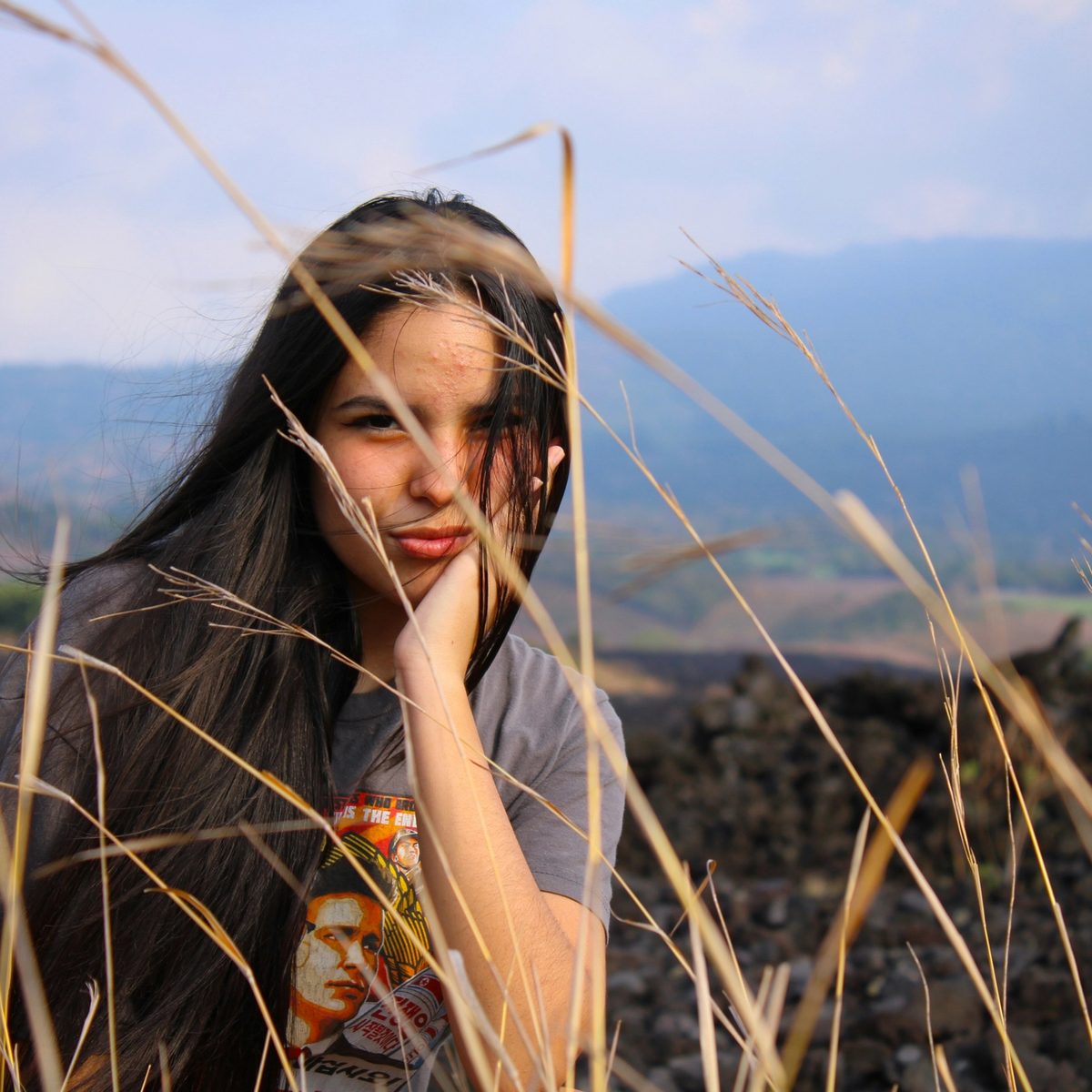 Woman in orange and white floral dress standing on brown grass field during daytime