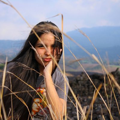 Woman in orange and white floral dress standing on brown grass field during daytime