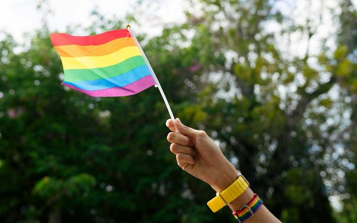 A hand waving a gay pride flag outdoors
