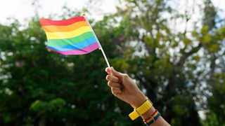 A hand waving a gay pride flag outdoors