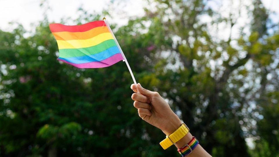 A hand waving a gay pride flag outdoors