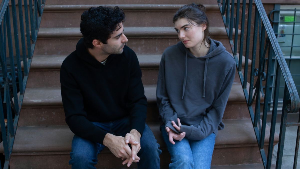 A couple is sitting on the stoop of a brownstone having an important conversation