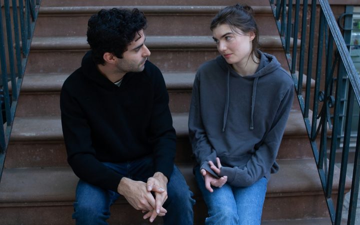 A couple is sitting on the stoop of a brownstone having an important conversation