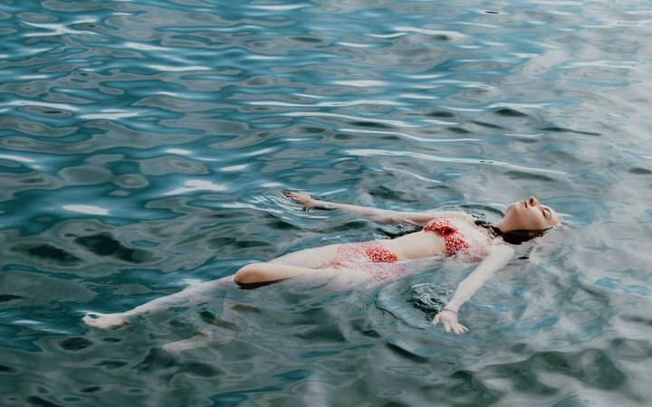 A swimmer floats on open waters, striking the delicate balance between resting and drowning.