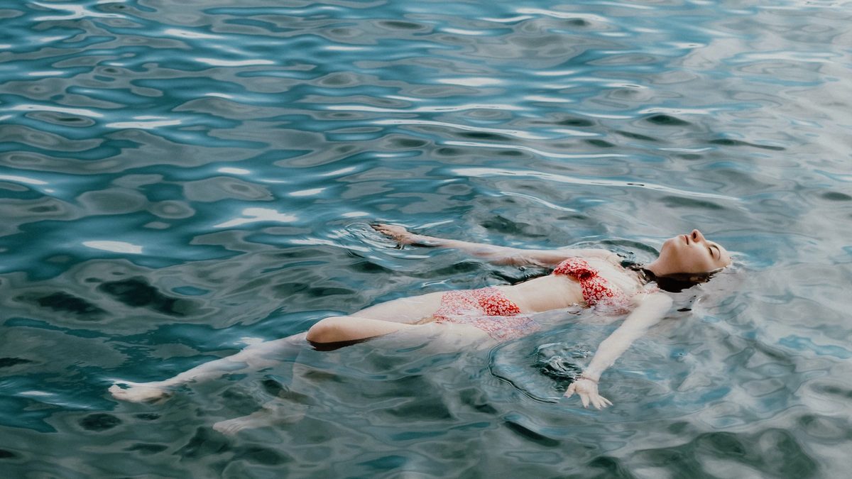 A swimmer floats on open waters, striking the delicate balance between resting and drowning.