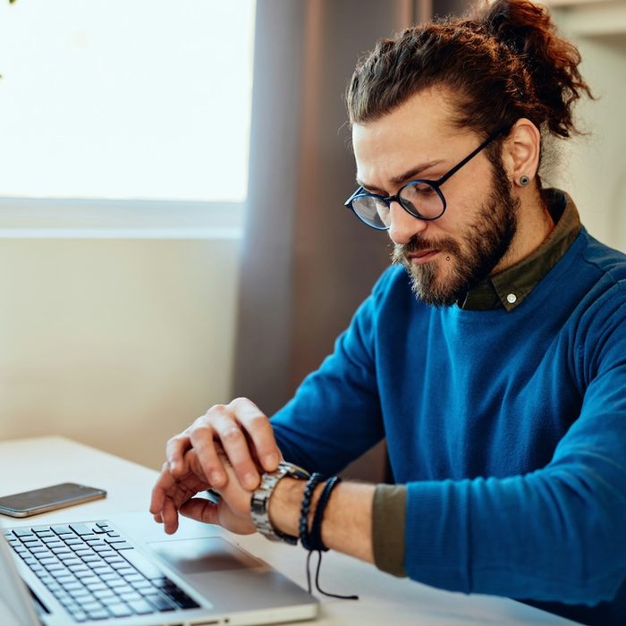 a therapist in a blue sweater is sitting at their desk, checking their watch after an online session