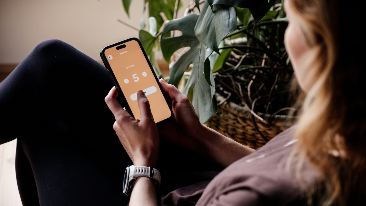 A woman sitting in a chair, using a meditation app to help reach her mental health goals.