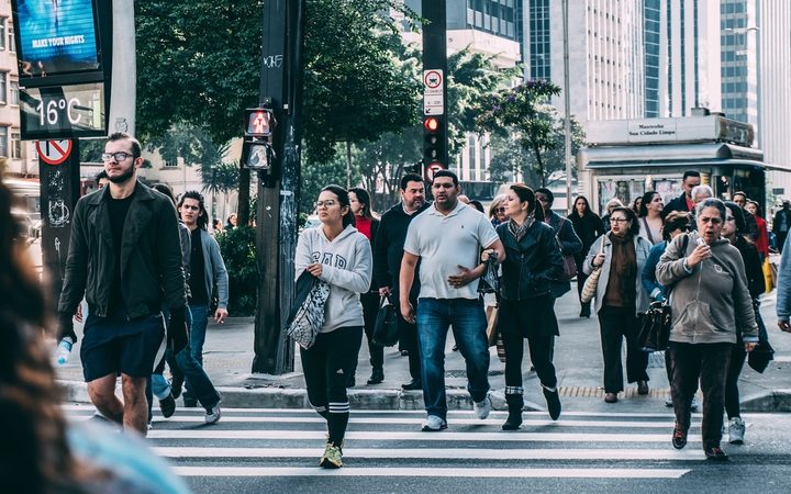 A collection of downtrodden folks of all walks of life, crossing a busy downtown crosswalk.