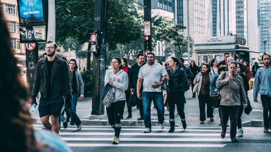 A collection of downtrodden folks of all walks of life, crossing a busy downtown crosswalk.