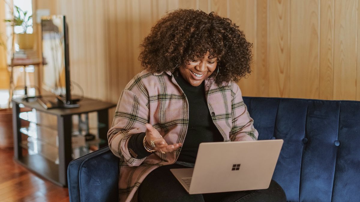 a hopeful, smiling woman sitting on her couch, talking to an online therapist