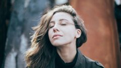 a calm, centered woman stands with her eyes closed outdoors, enjoying the late afternoon sun