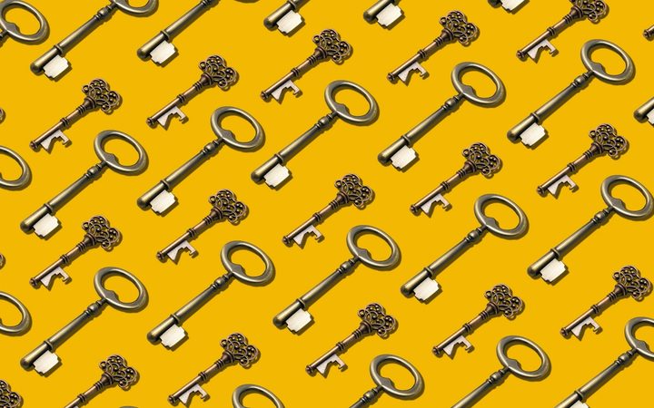 Many ornate brass keys laid flat in a perfectly repeating pattern on a marigold backdrop.