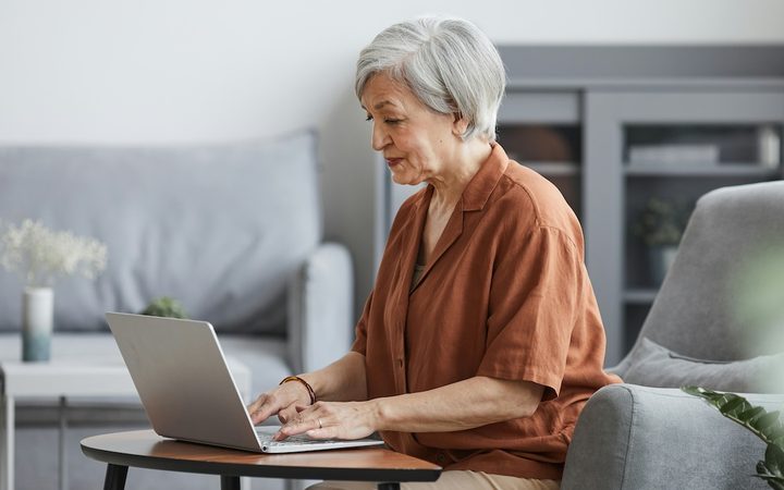 a stylish older woman is on her laptop at home, searching for a therapist who accepts medicare