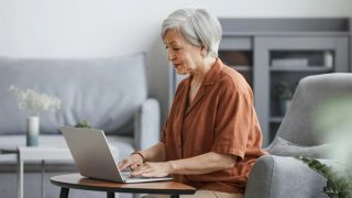 a stylish older woman is on her laptop at home, searching for a therapist who accepts medicare