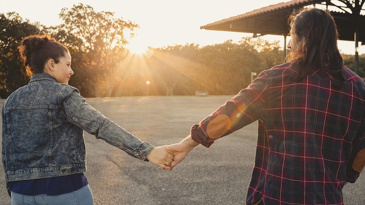 A hesitant but hopeful couple walking at sunset, holding hands at arm's length