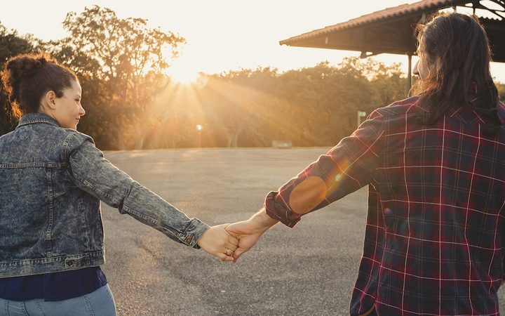 A hesitant but hopeful couple walking at sunset, holding hands at arm's length
