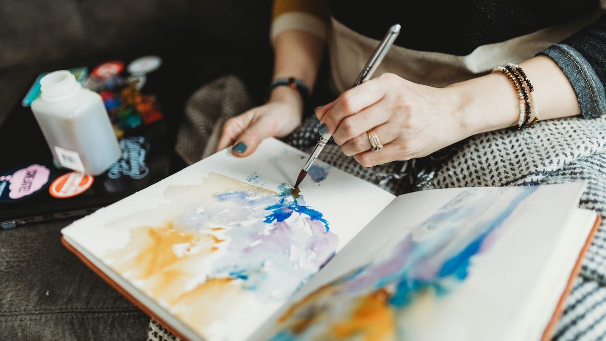 A woman using watercolors to pain an abstract image into a journal