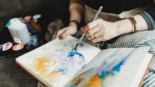 A woman using watercolors to pain an abstract image into a journal
