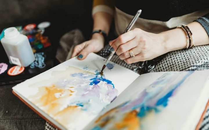 A woman using watercolors to pain an abstract image into a journal