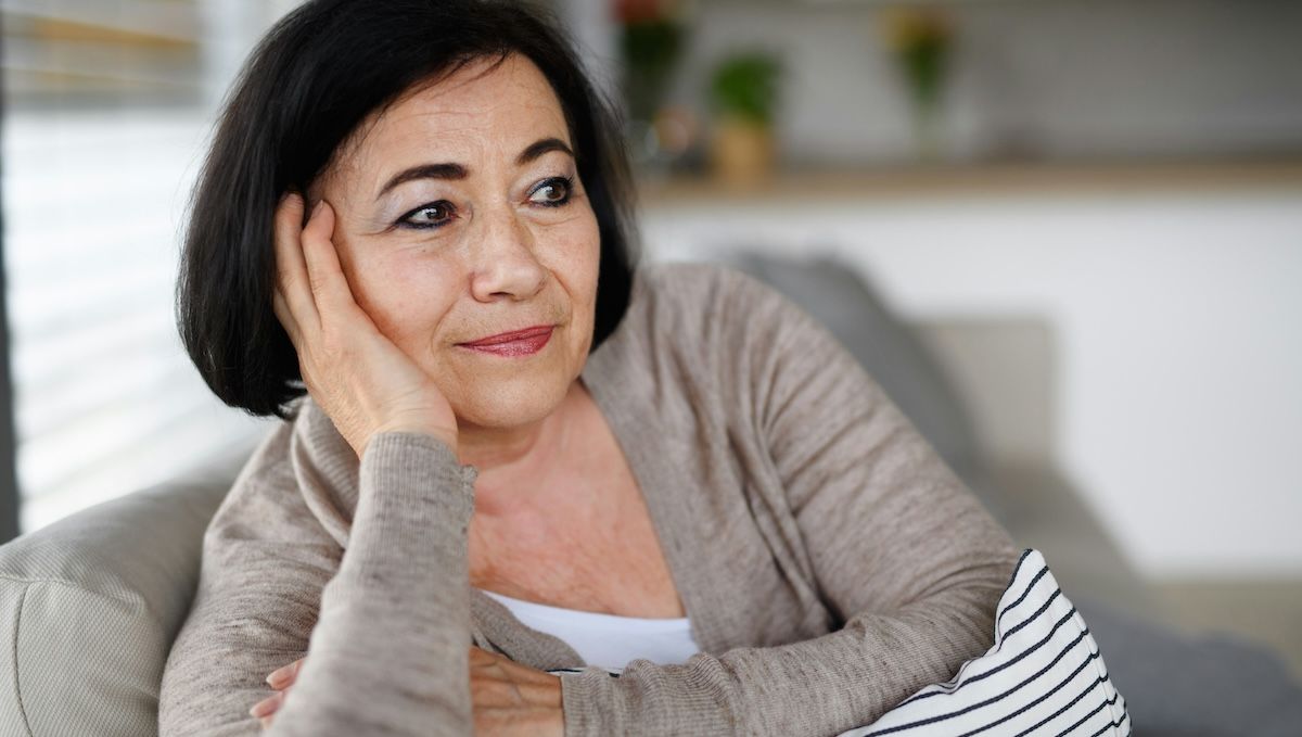 a sixty-something woman sits on the couch at home looking thoughtful as she wonders if a younger therapist could really help her