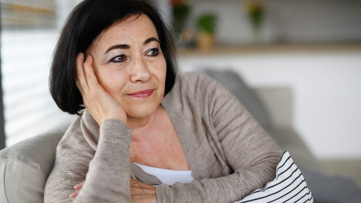 a sixty-something woman sits on the couch at home looking thoughtful as she wonders if a younger therapist could really help her