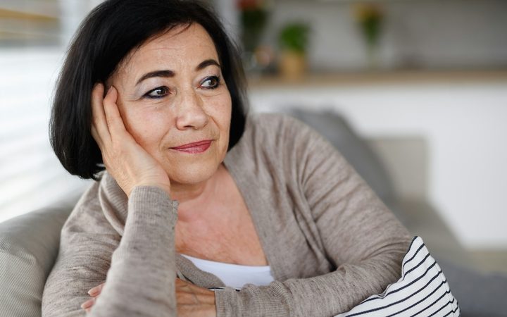 a sixty-something woman sits on the couch at home looking thoughtful as she wonders if a younger therapist could really help her