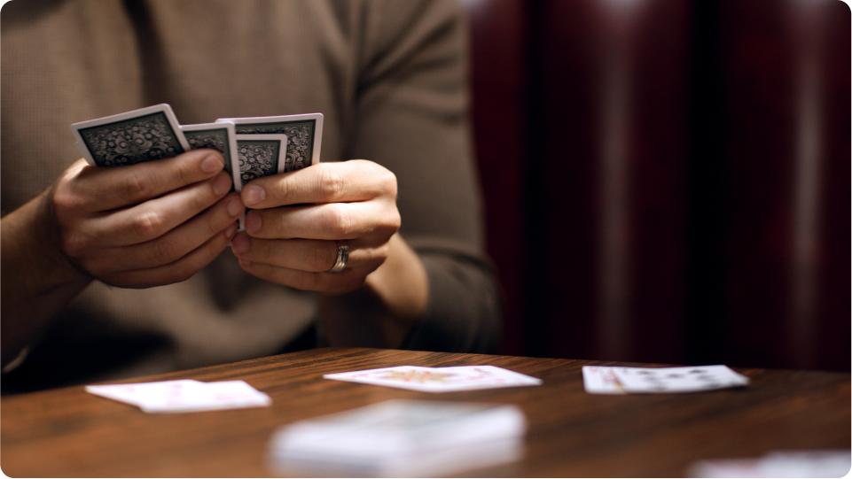 Woman with wedding ring on holding playing cards alone
