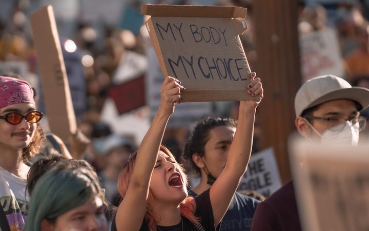 An LA woman protests the US Supreme Court's reversal of Roe v Wade, chanting while holding a cardboard sign that says "My Body My Choice."