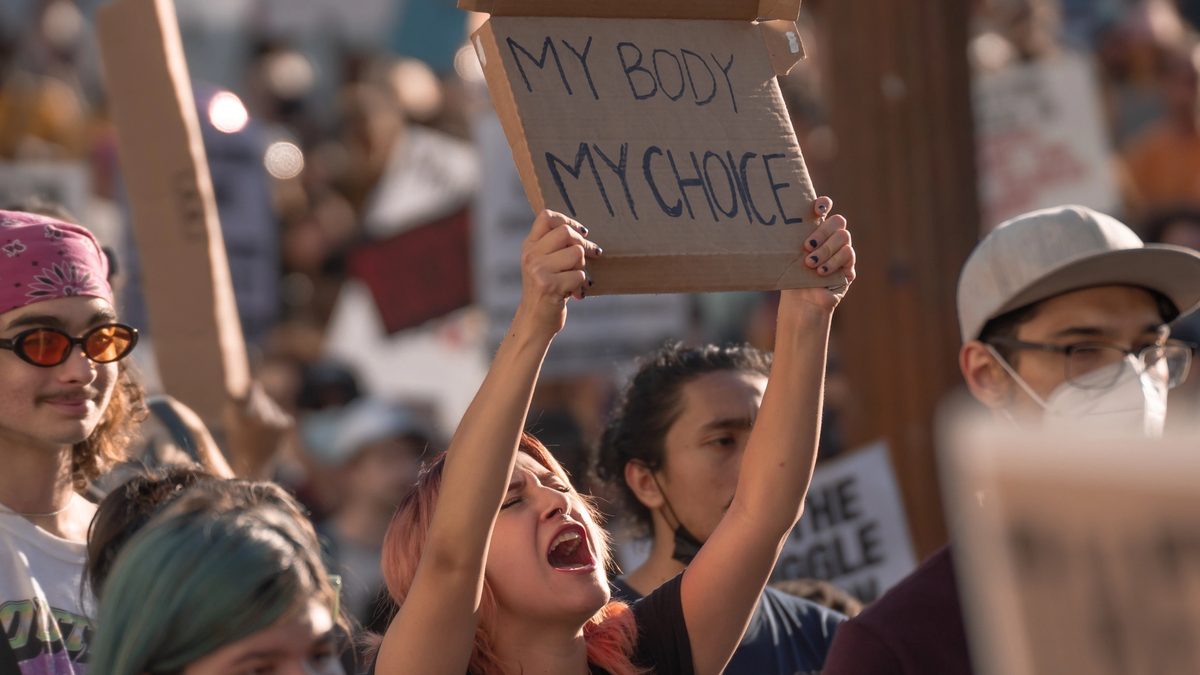 An LA woman protests the US Supreme Court's reversal of Roe v Wade, chanting while holding a cardboard sign that says "My Body My Choice."