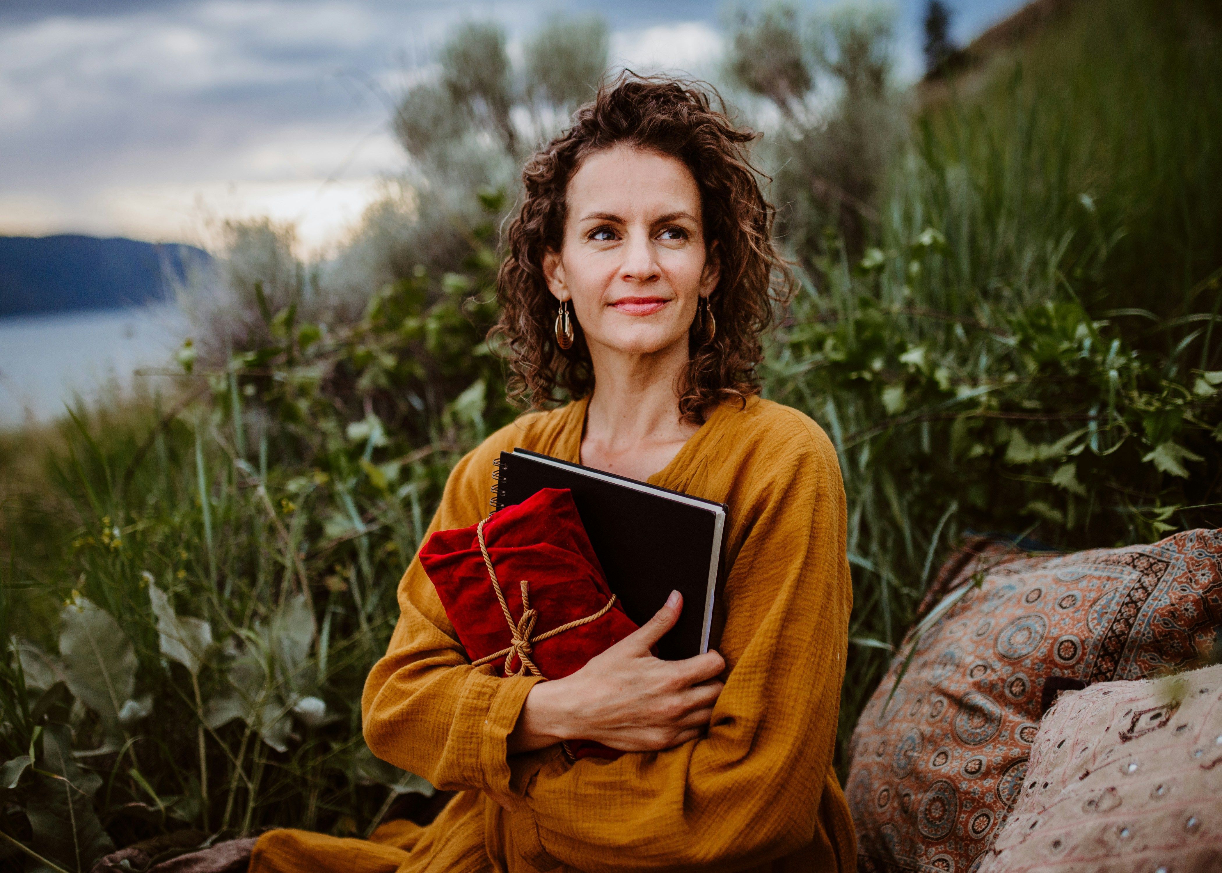 Woman journalling and holding fabric wrapped gift as she sits on the shores of a lake