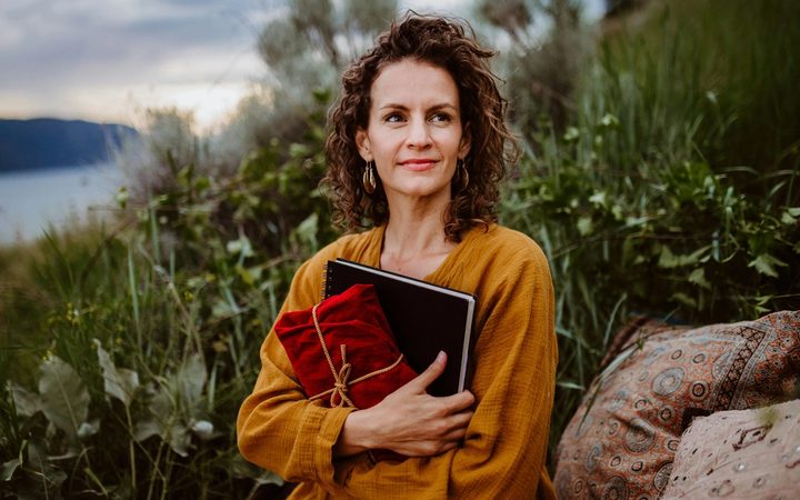Woman journalling and holding fabric wrapped gift as she sits on the shores of a lake