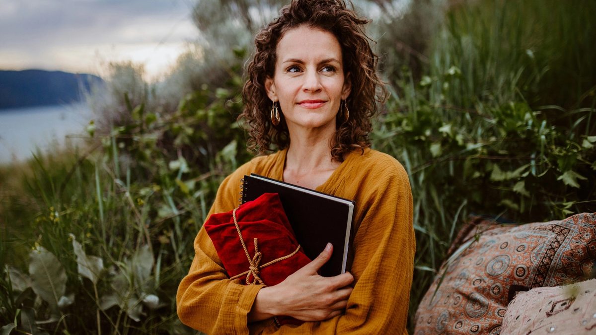 Woman journalling and holding fabric wrapped gift as she sits on the shores of a lake