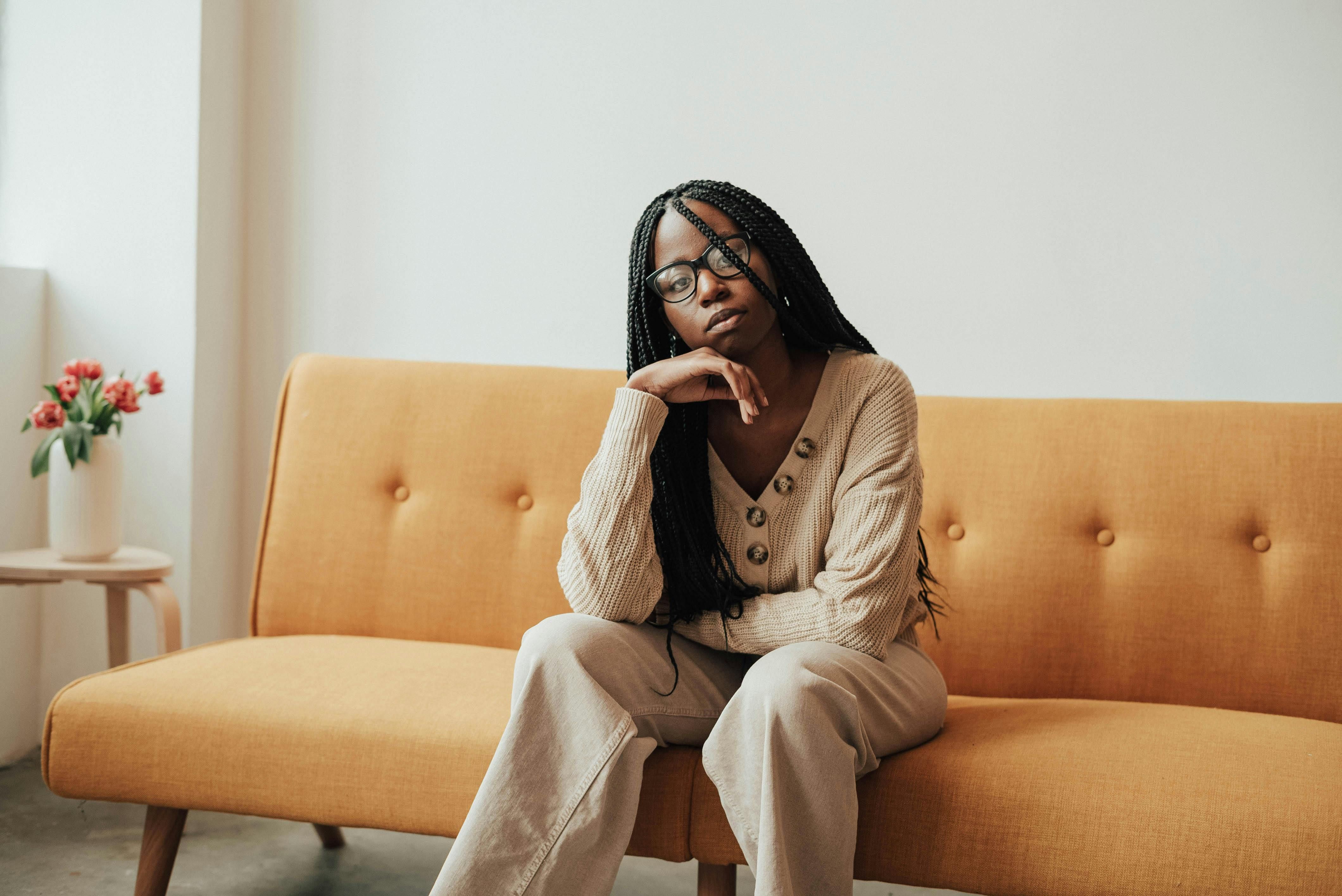 A Black female therapist with box braids sits on a midcentury sofa upholstered in tangerine linen.
