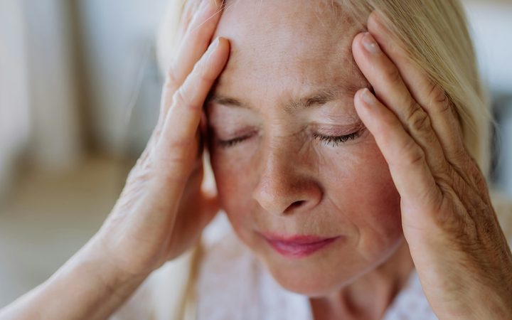An older woman suffering with chronic pain holding her face in her hands