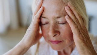 An older woman suffering with chronic pain holding her face in her hands