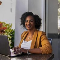 Dr. Shaenor sits at a table, hands poised above the keyboard of a laptop, smiling to camera.