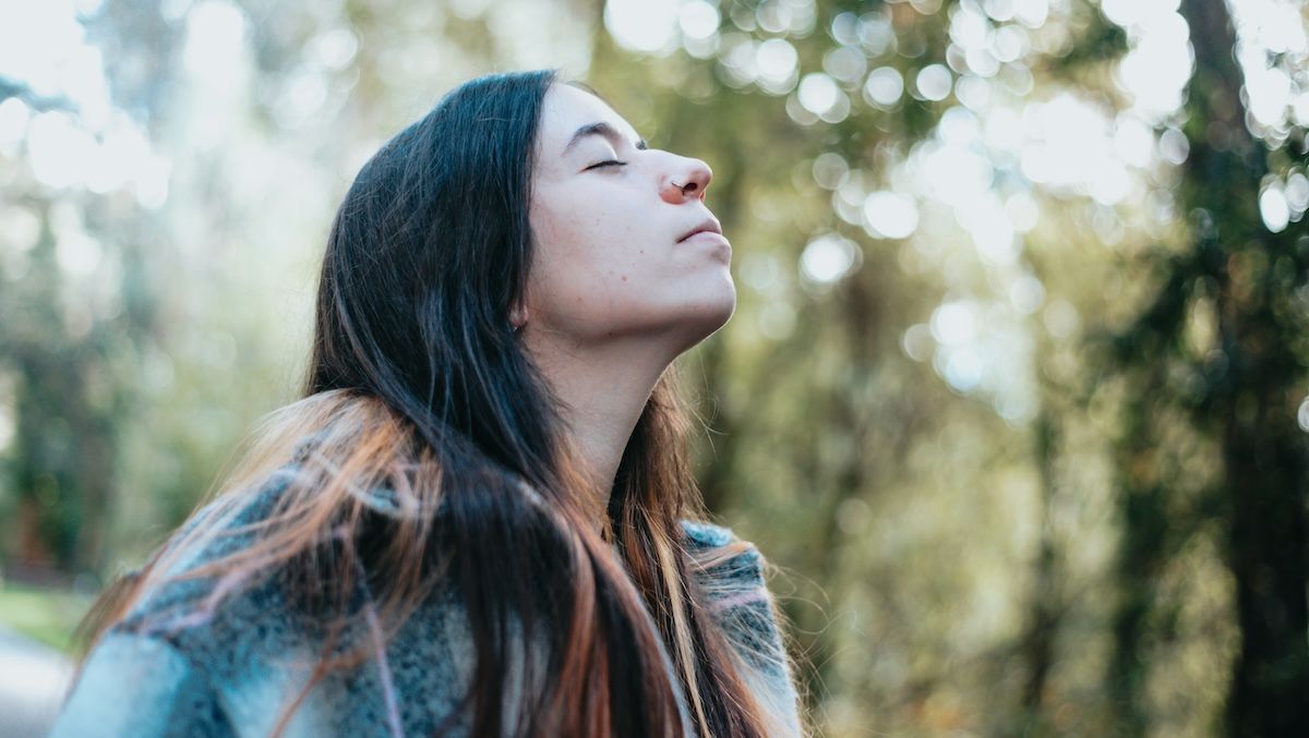 A woman stopping to breathe the fresh air as she walks through sunlit trees 