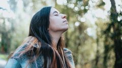 A woman stopping to breathe the fresh air as she walks through sunlit trees