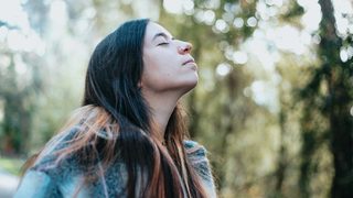 A woman stopping to breathe the fresh air as she walks through sunlit trees