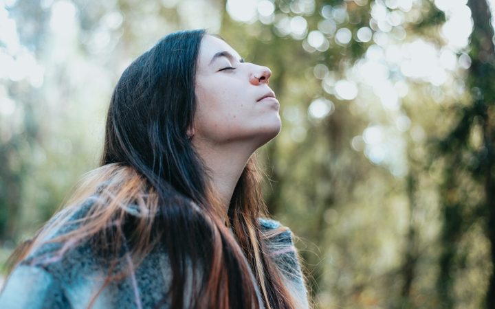 A woman stopping to breathe the fresh air as she walks through sunlit trees