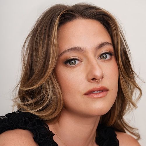 Haley Jakobson, a white femme with long brown wavy hair gazes into the camera with a curious gaze.