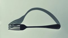a fork is shown on a light green background, next to its oddly shaped shadow