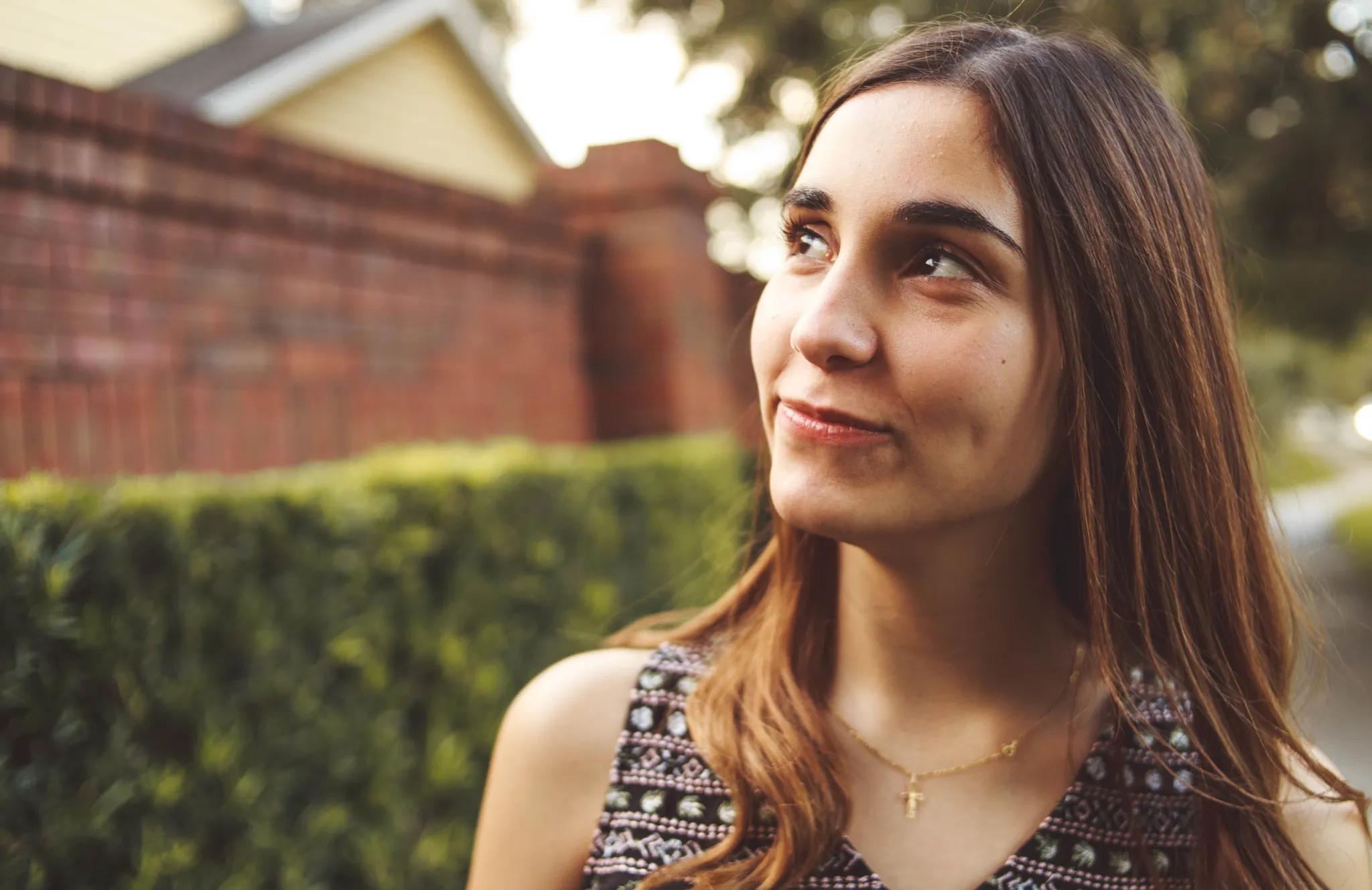 A young woman looks up, hopefully, while walking through the neighborhood.