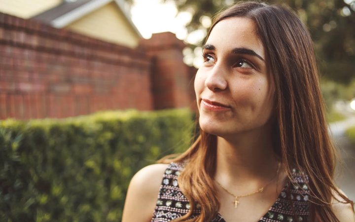 A young woman looks up, hopefully, while walking through the neighborhood.