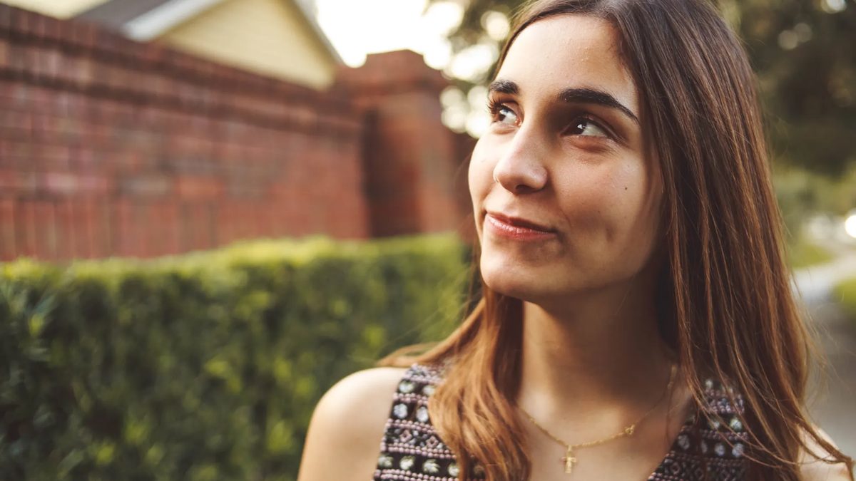 A young woman looks up, hopefully, while walking through the neighborhood.