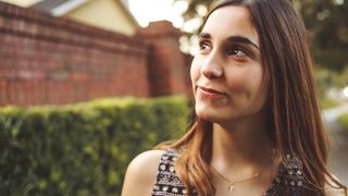 A young woman looks up, hopefully, while walking through the neighborhood.