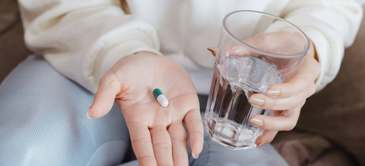 An open hand holding a single capsule beside a glass of water