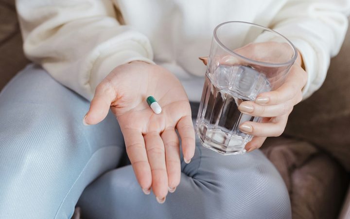 A close-up of a seated woman holding a pill in one hand and a glass of water in the other