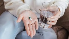 A close-up of a seated woman holding a pill in one hand and a glass of water in the other