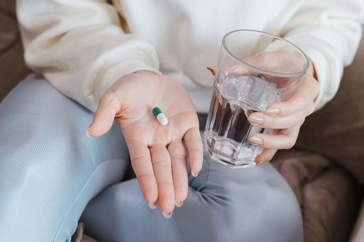 A close-up of a seated woman holding a pill in one hand and a glass of water in the other